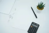 A calculator beside a pen on white printer paper.