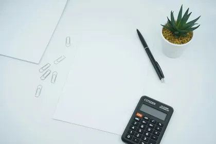 A calculator beside a pen on white printer paper.